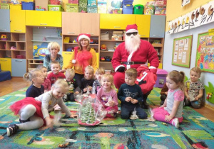 Grupa dzieci siedzi na dywanie z Mikołajem oraz ze swoimi paniami